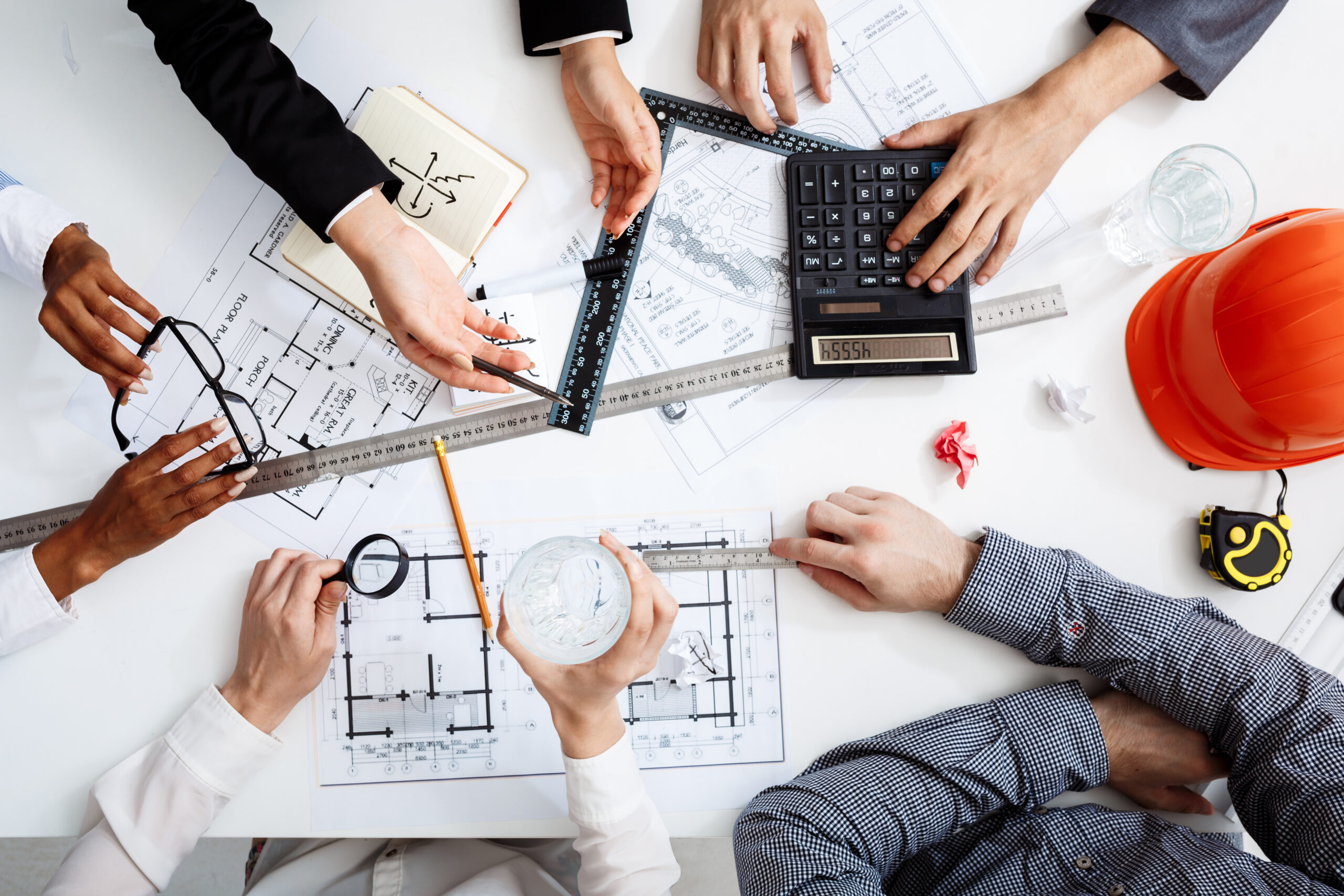 The ROI of switching to electrical project management software illustrated by a project team reviewing electrical drawings, measurements, and costs around a planning table.