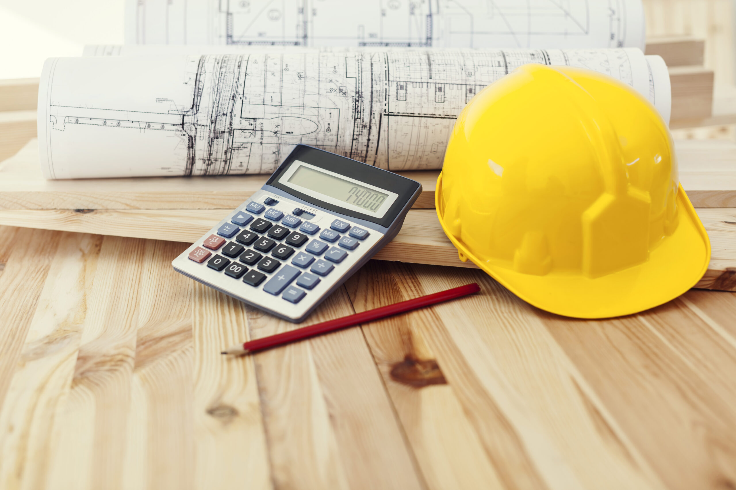 Desk scene showing plans, calculator and hard hat to illustrate why electrical project management software is essential for modern electrical teams.