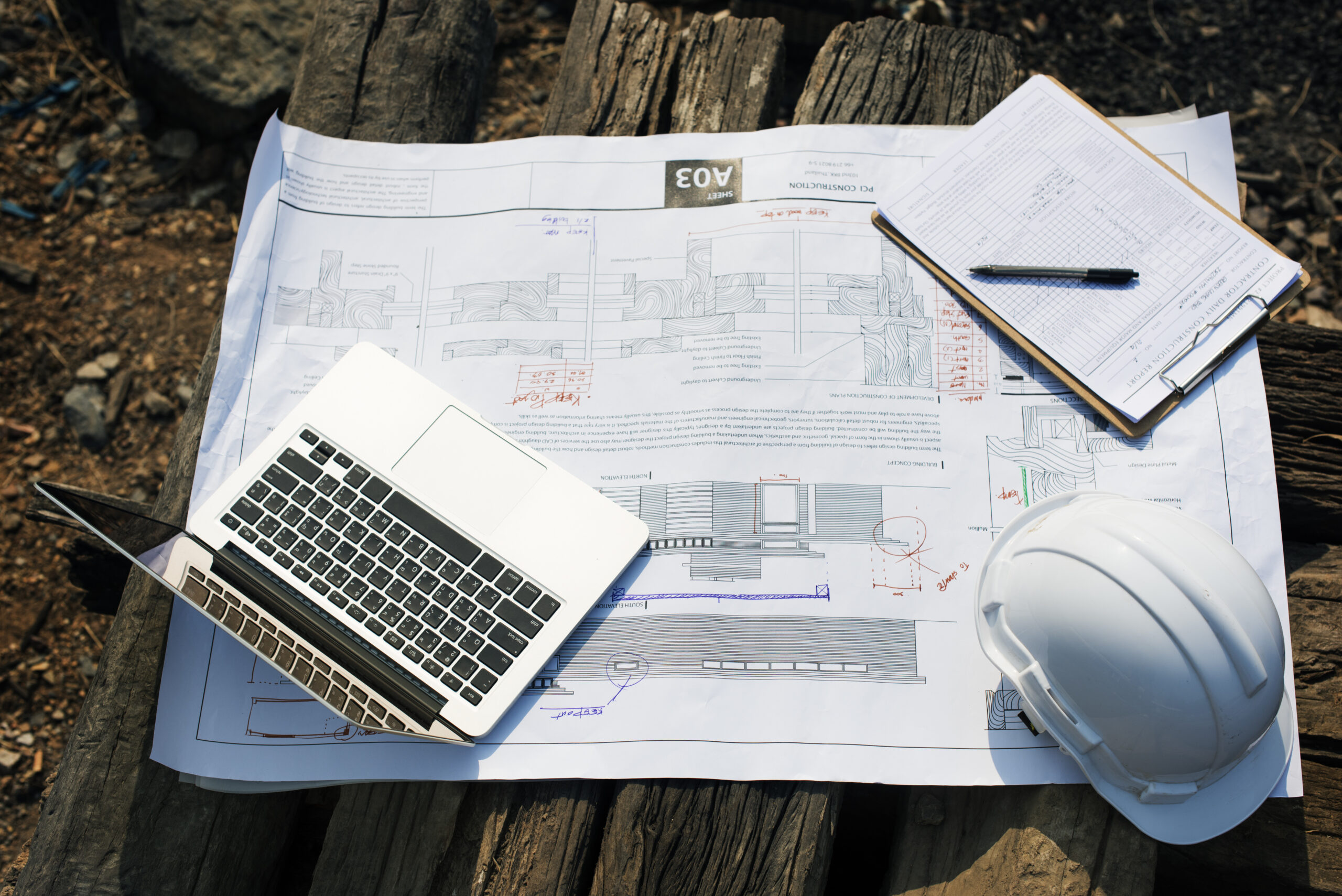 Top-down view of blueprints, a laptop, and a hard hat, highlighting where common electrical mistakes electrical project management software solves through better planning.