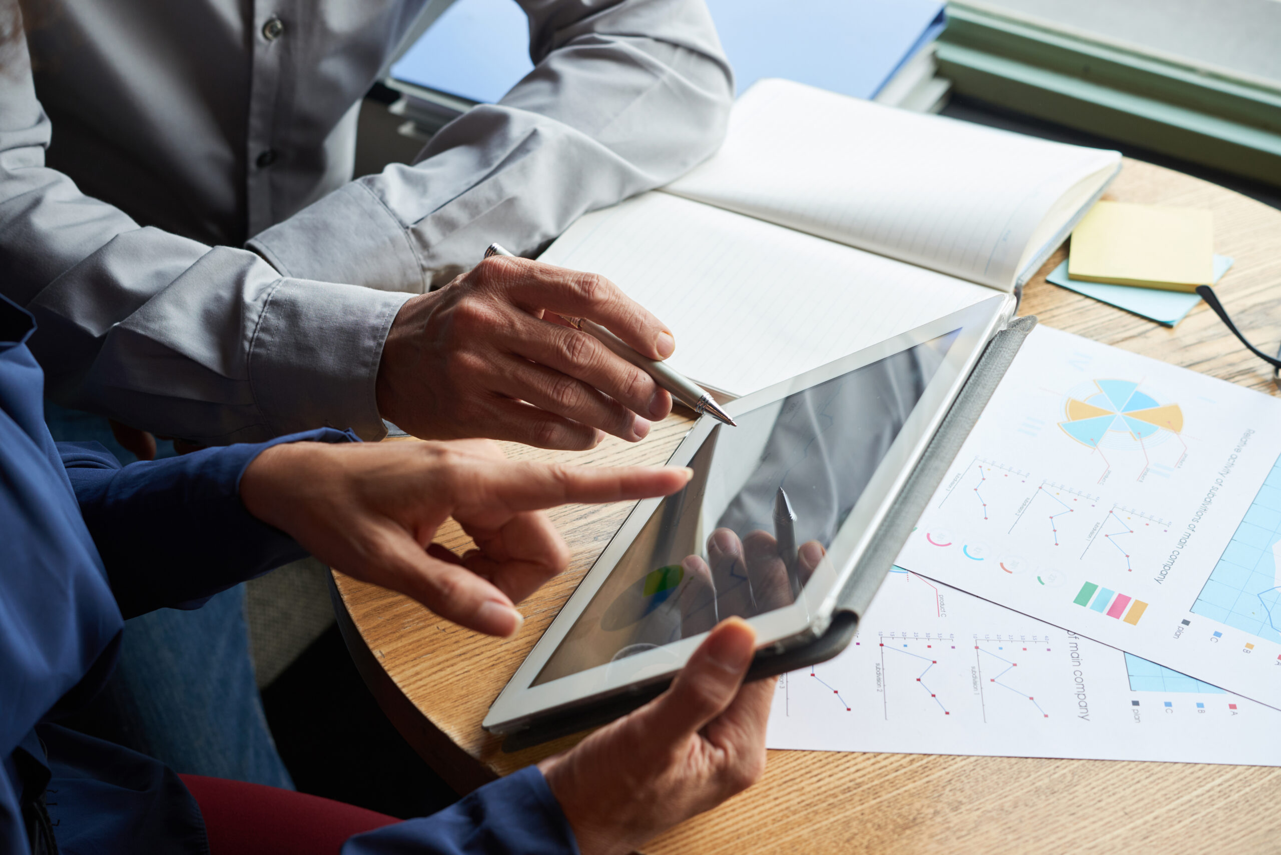Two professionals analysing data charts on a tablet, demonstrating top features to look for in electrical project management software like real-time reporting and analytics.