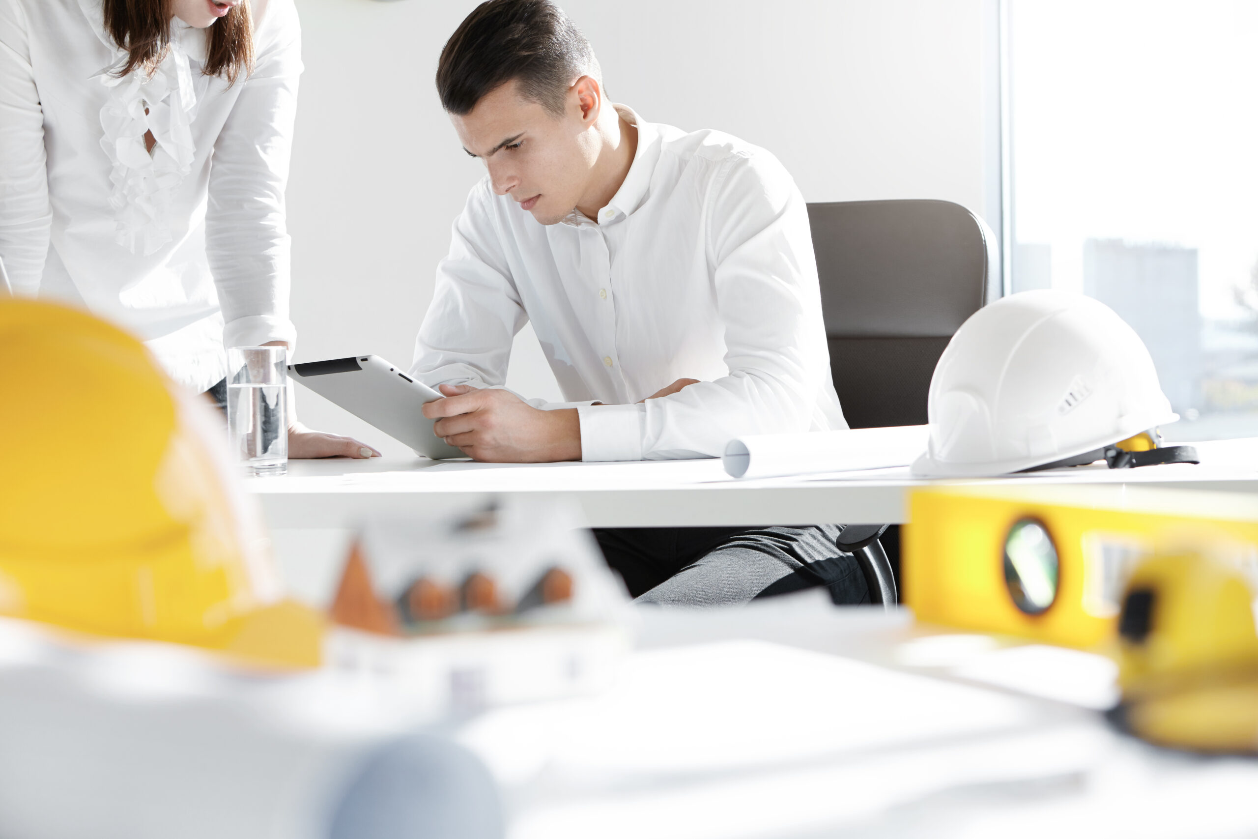 Engineers reviewing a tablet beside hard hats and project plans, illustrating common MEP mistakes MEP project management software solves.