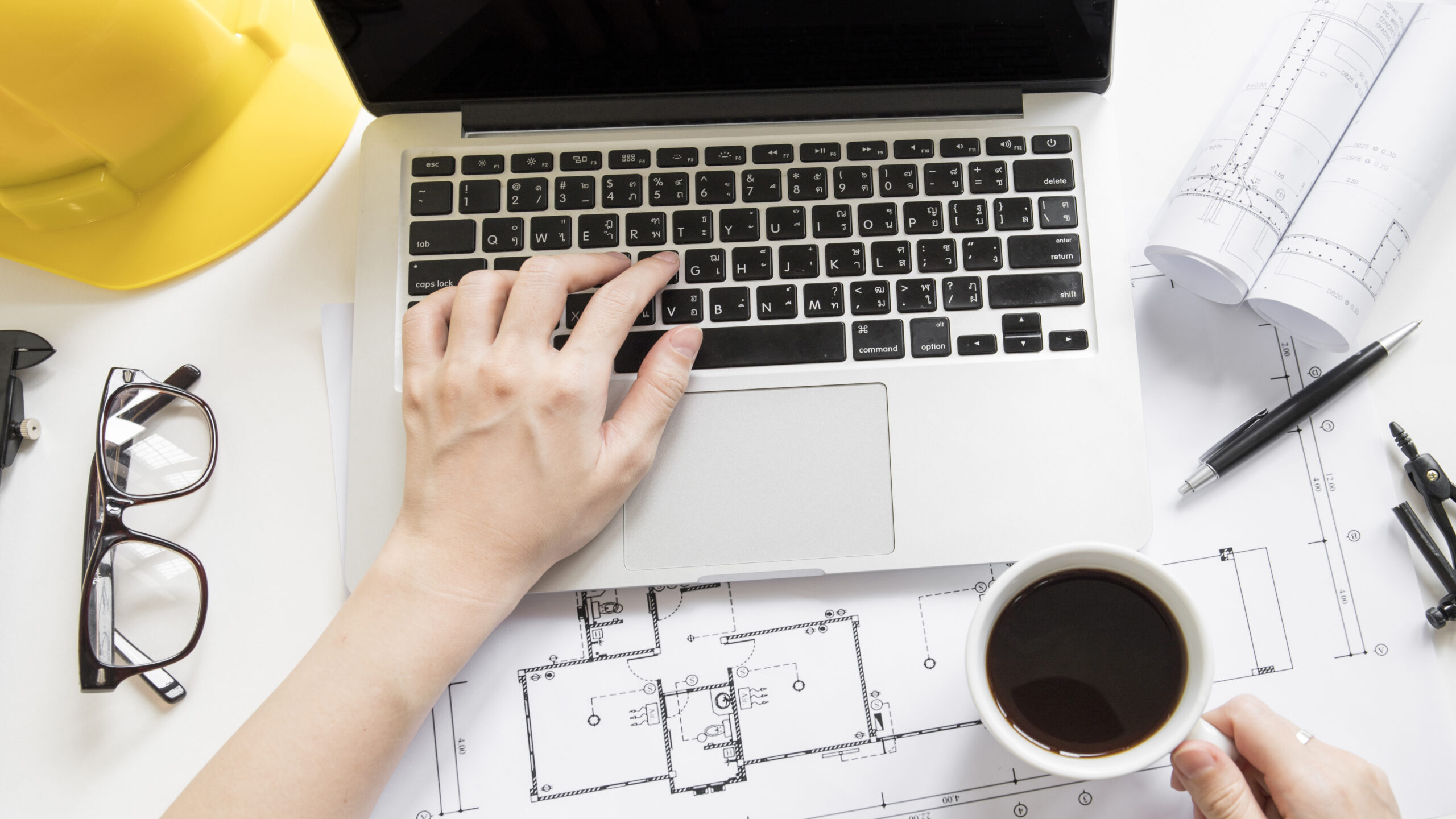 Laptop, hard hat, and construction drawings on a desk, highlighting top features to look for in MEP project management software.