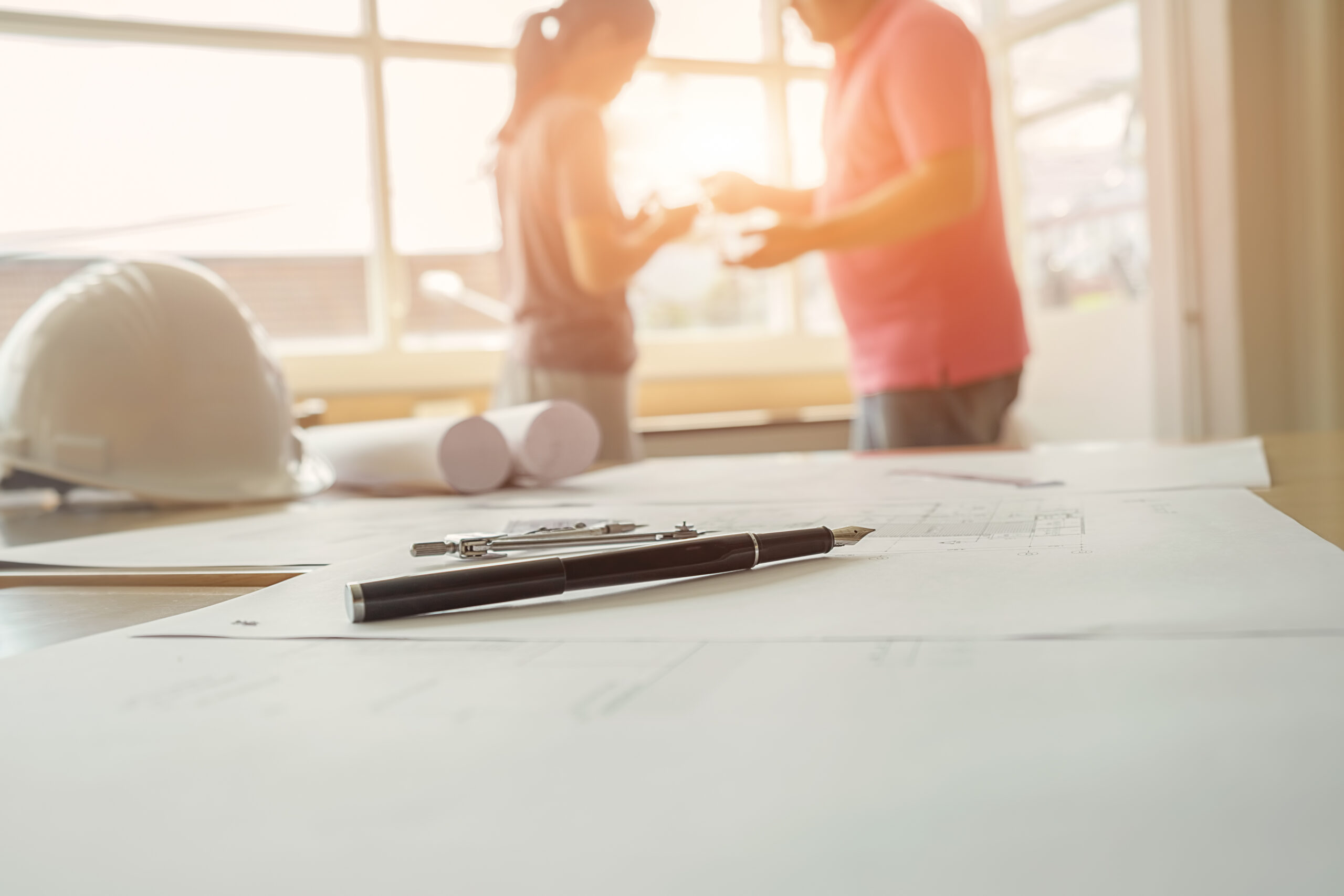 Construction drawings and tools on a desk during a team discussion, showing how to train staff on MEP project management software.