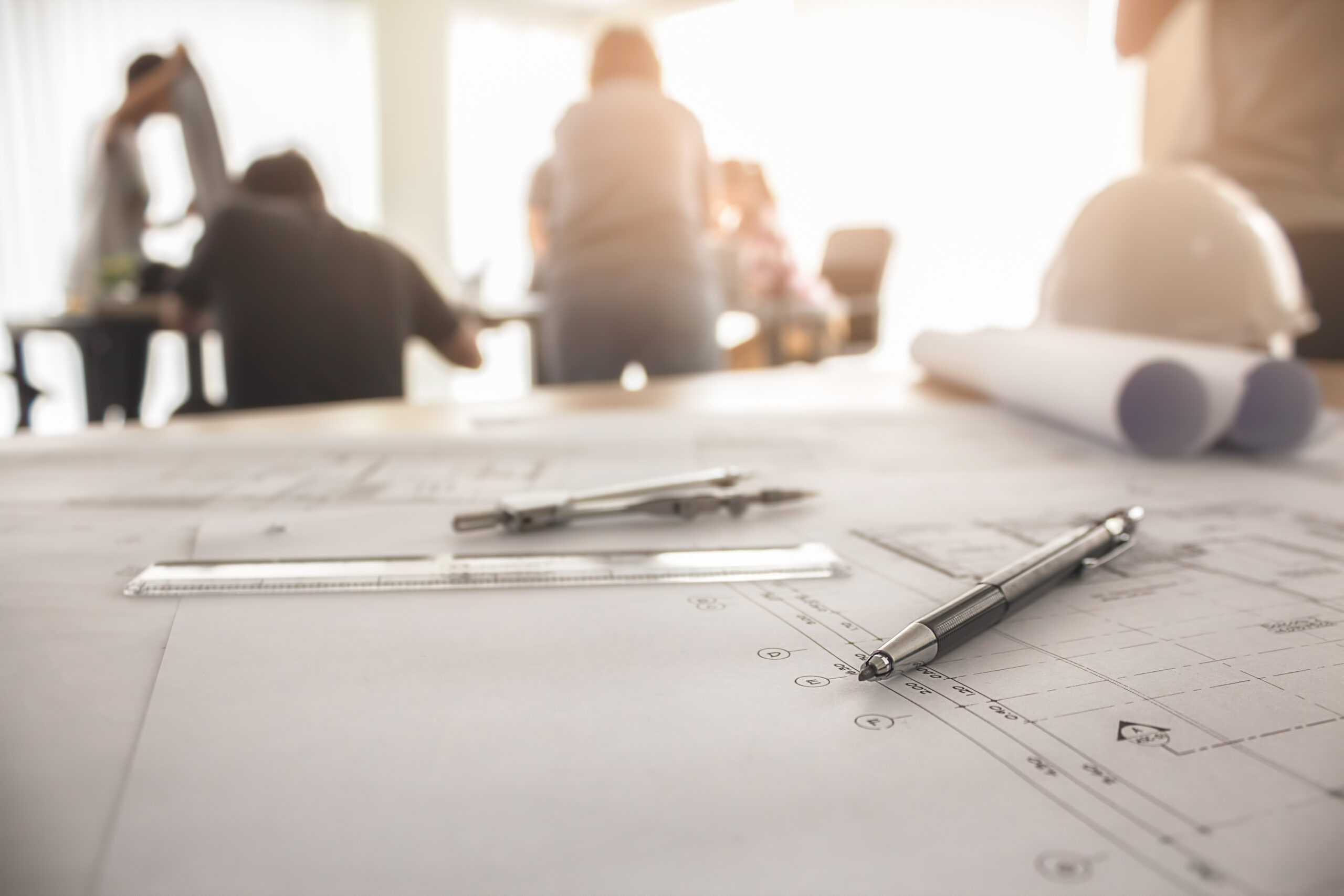 Construction plans and tools on a desk during a team meeting, showing how SMEs benefit from MEP project management software.