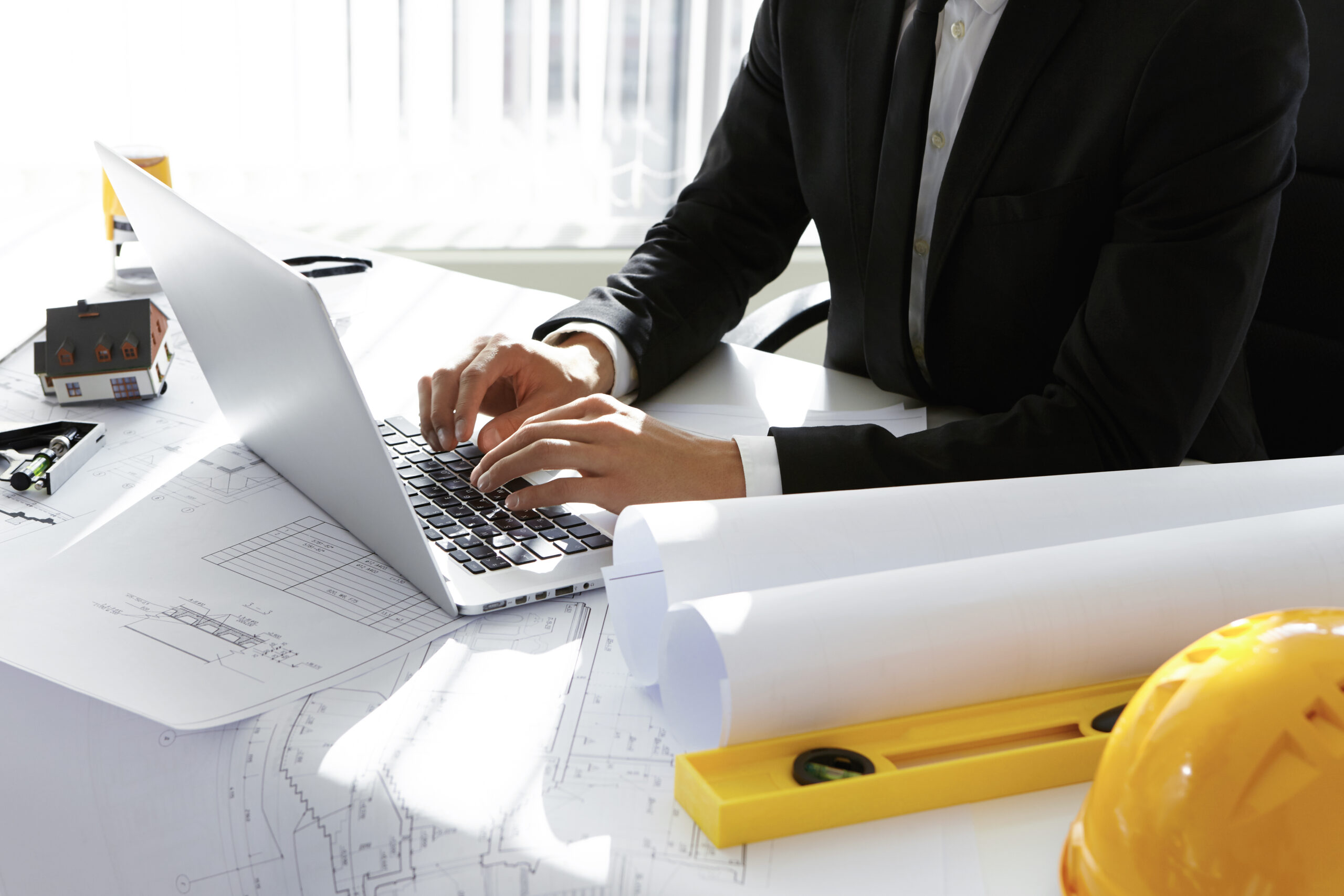 Professional reviewing digital plans on a laptop with construction drawings and tools, highlighting MEP project management software vs manual processes: a full comparison.
