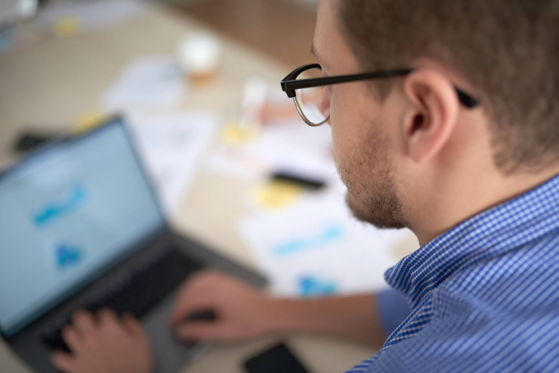 A project manager working on a laptop with documents and notes on the desk, illustrating the top features to look for in mechanical project management software.